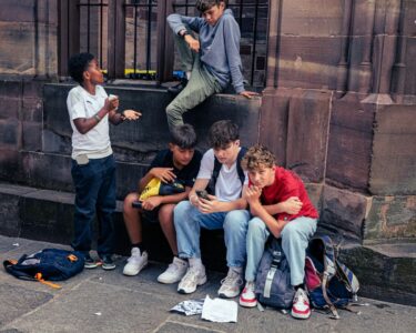 A group of boys hanging out, looking at a mobile phone